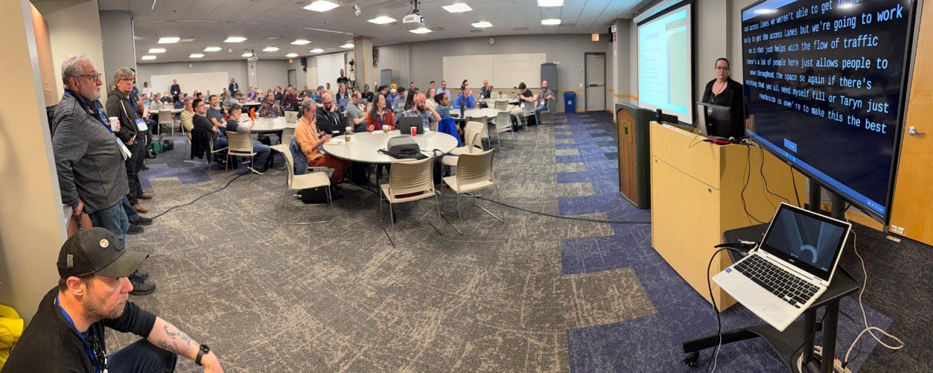 Norah Shannon Medlin welcomes the delegates at Midwest Drupal Camp (MidCamp) 2025. Live caption can be seen in the screen to her left. 