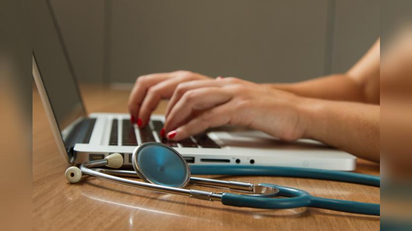 A person working on the laptop with a stethoscope beside 