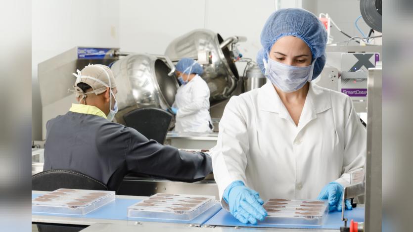 Three people inside a factory wearing masks and coats