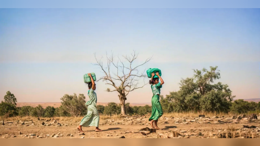 Two women carrying water through a barren land