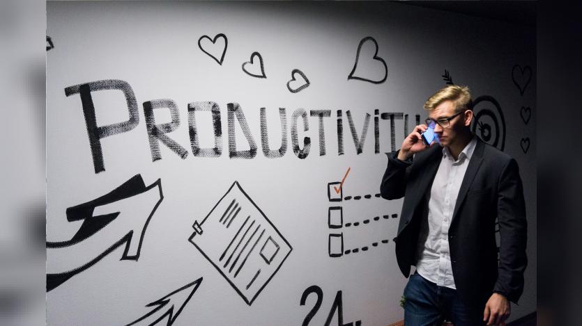 A man talking over the mobile phone passing by a wall with graffity that says about productivity