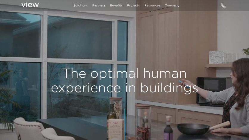 Website header with navigation and hero section showing two people talking by a window overlooking a lake, text 'The optimal human experience in buildings'