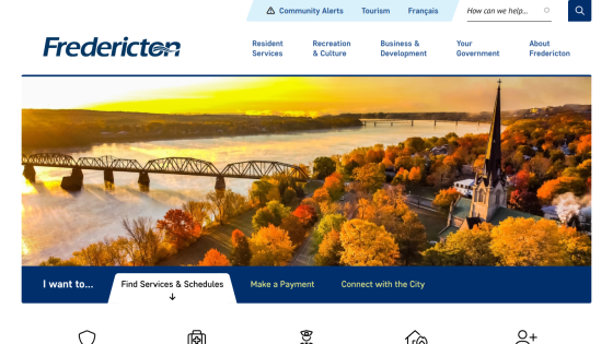Fredericton city website with navigation links, search bar, and autumn aerial view of river, bridge, and church steeple