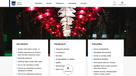 Ogres novads website with navigation menu and sections for Aktualitātes, Pakalpojumi, and Pašvaldība under illuminated umbrella installation
