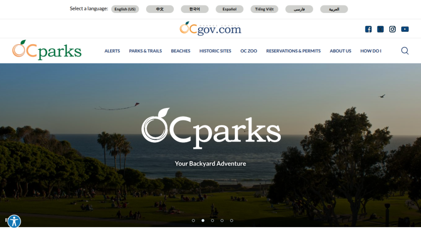 OC Parks website homepage with navigation menu and a scenic park view by the ocean under a clear sky