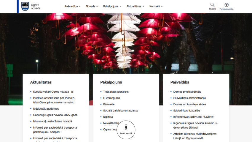 Ogres novads website with navigation menu and sections for Aktualitātes, Pakalpojumi, and Pašvaldība under illuminated umbrella installation