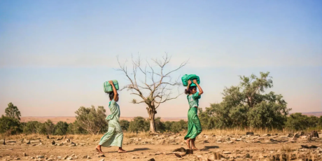 Two women carrying water through a barren land