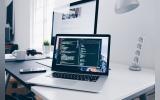 A MacBook with lines of code on its screen on a busy desk