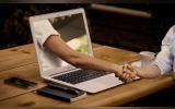 a man shaking hands with a hand projecting out of a laptop screen